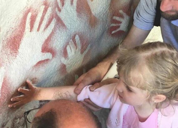 Niña observando pinturas rupestres con ayuda de adultos